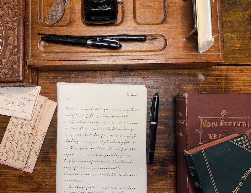 Vintage wooden desk with handwritten letters, a fountain pen, and an ink bottle among old books and papers (top view).