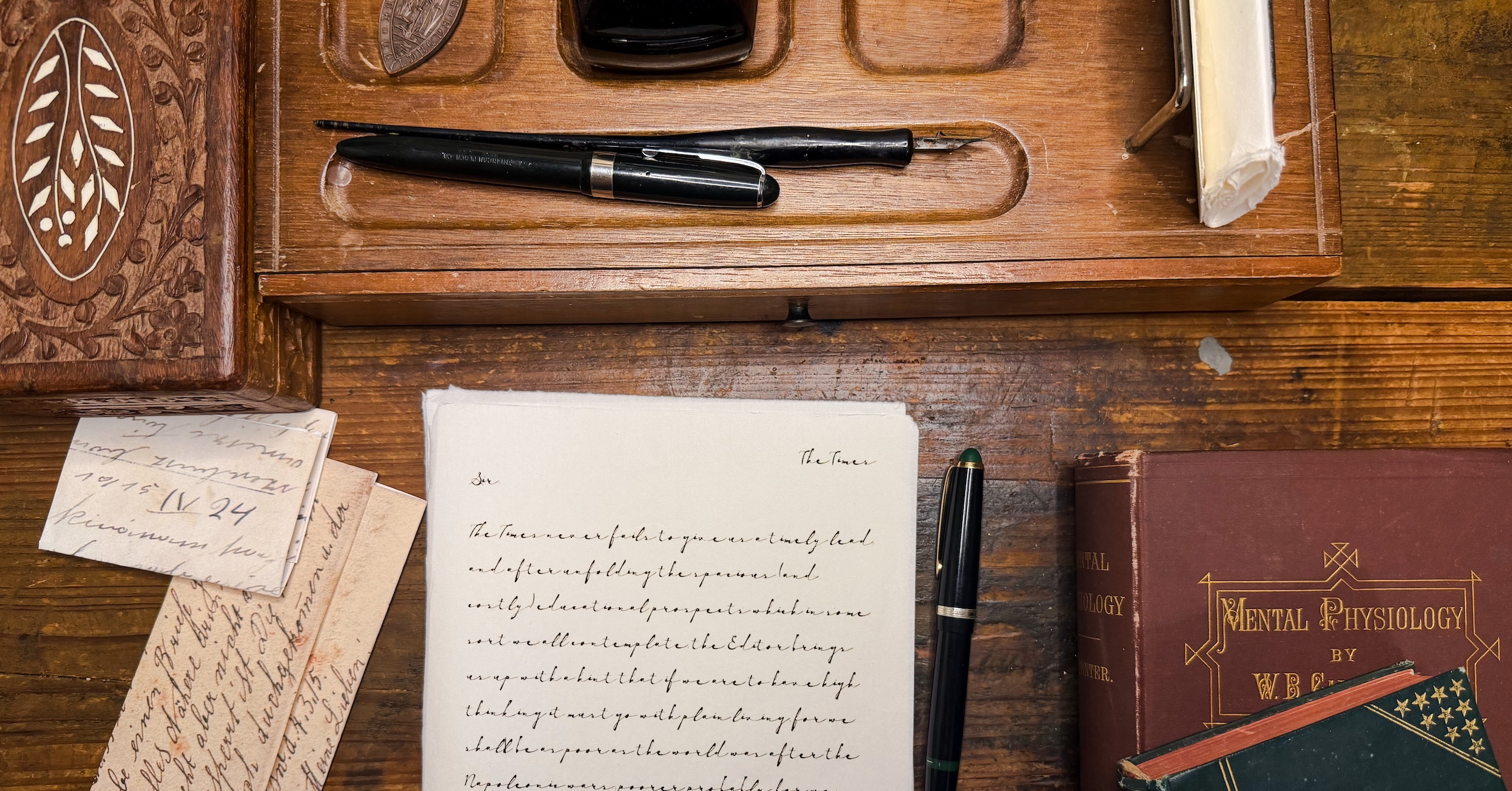 Vintage wooden desk with a fountain pen, handwritten notes, and antique books scattered about.
