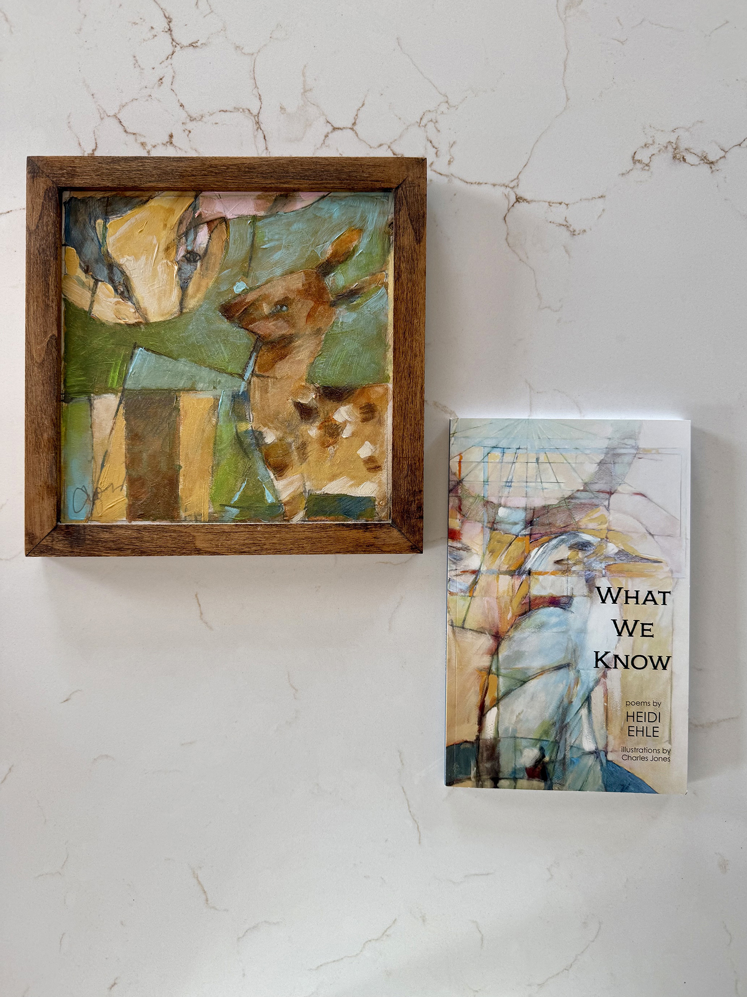 Abstract, colorful painting in a wooden frame leaning on a marble-surfaced wall, beside a booklet titled 'What We Know'.