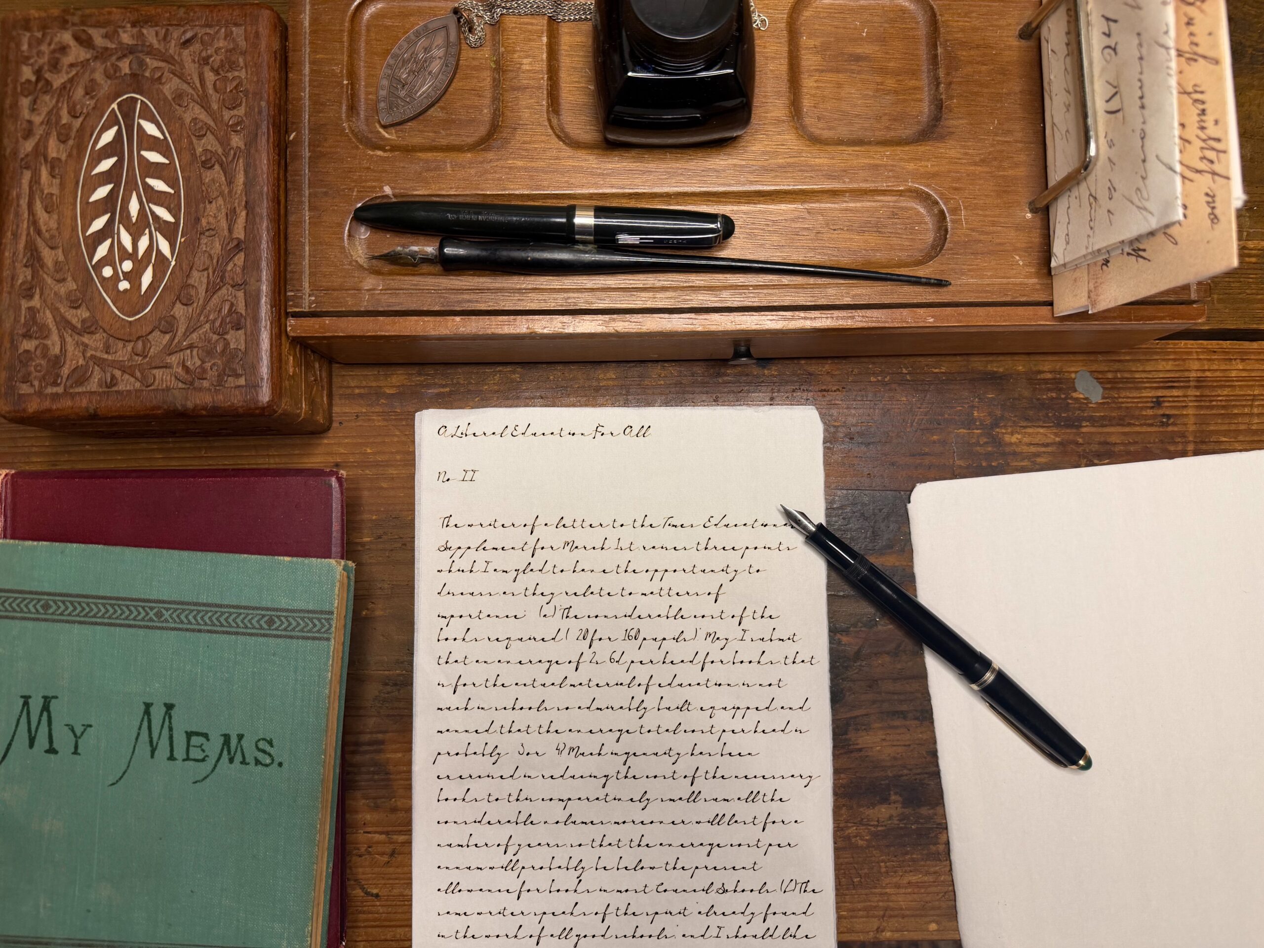 Top view of a vintage desk with fountain pens, an ink bottle, and handwritten letters among old books on a wooden surface.