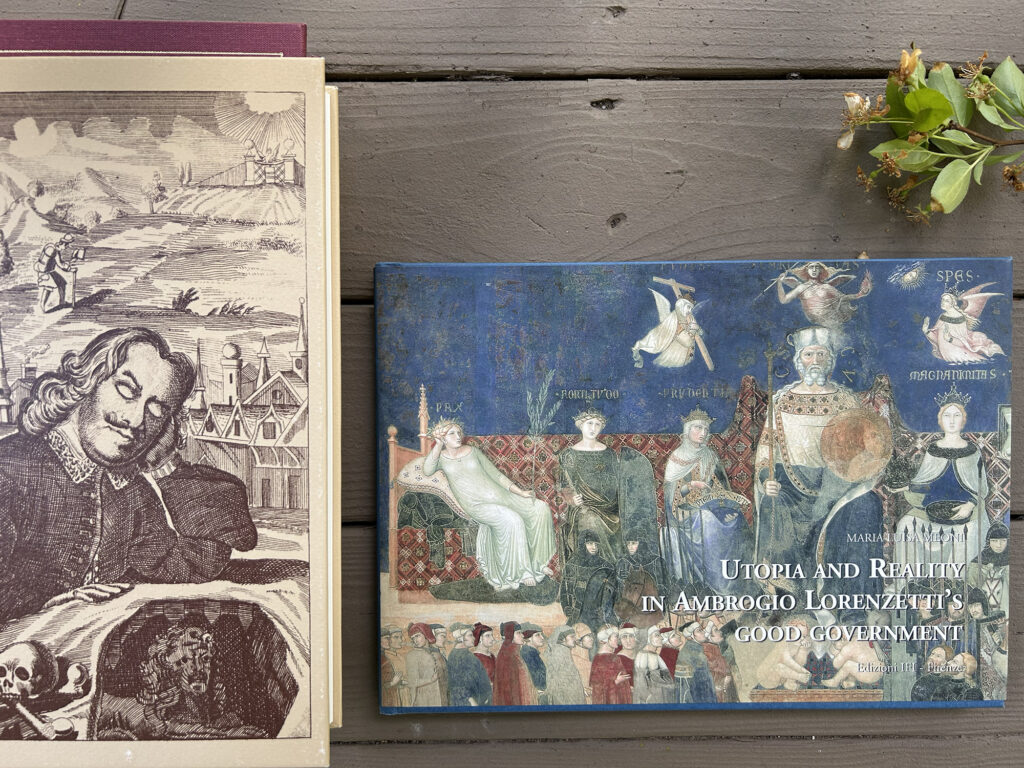 Two antique books lie on a wooden surface; the left book shows a sepia engraving of a man writing, the right blue volume features medieval figures and the title Utopia and Reality.