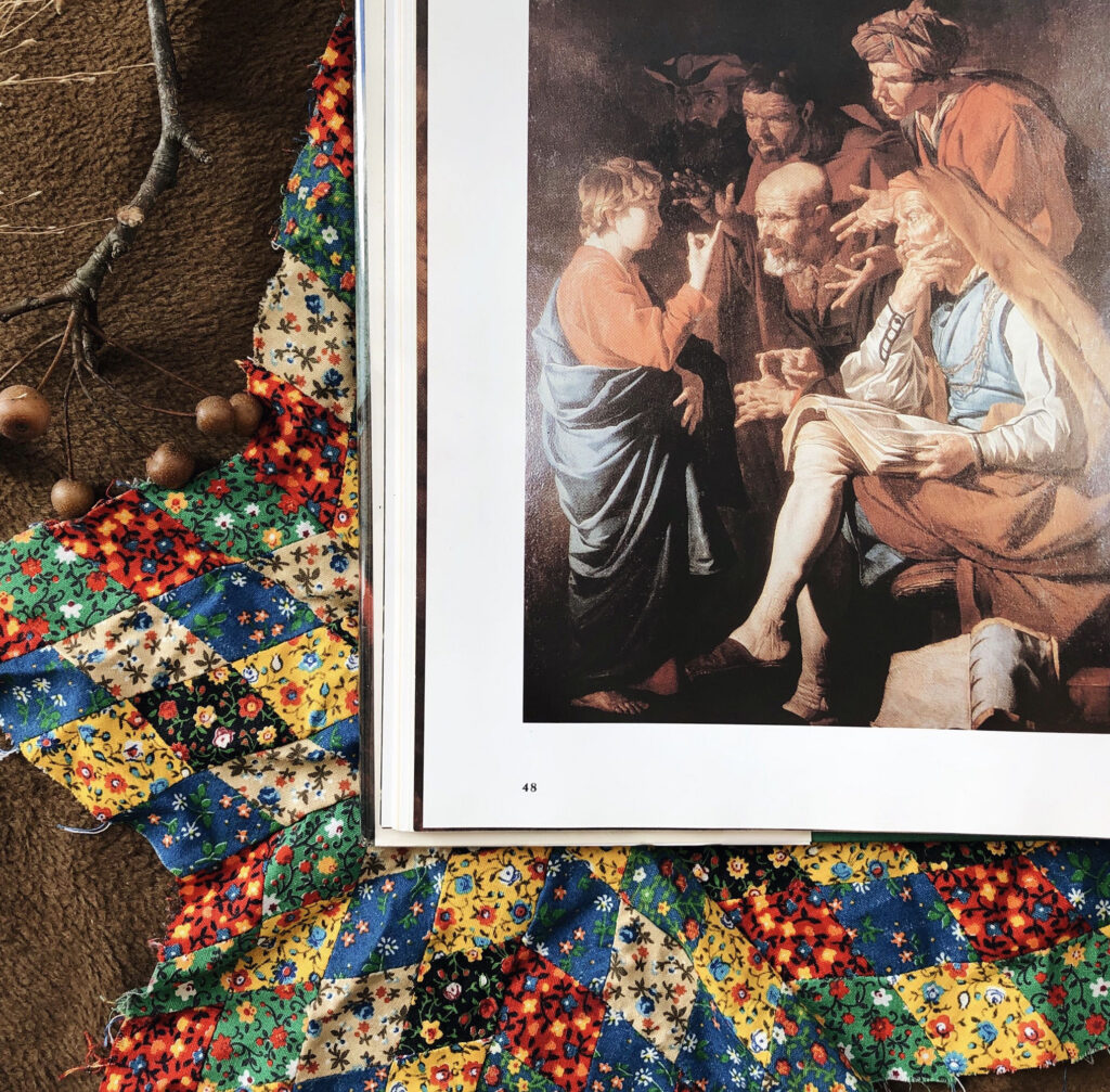 Open book showing a Renaissance-style painting of people at a table on the right page, with colorful floral fabric on the left.