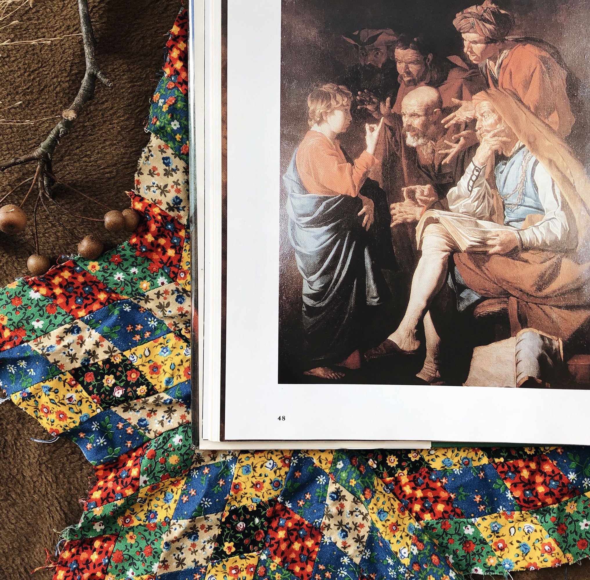 Open book showing a Renaissance-style painting of people at a table on the right page, with colorful floral fabric on the left.