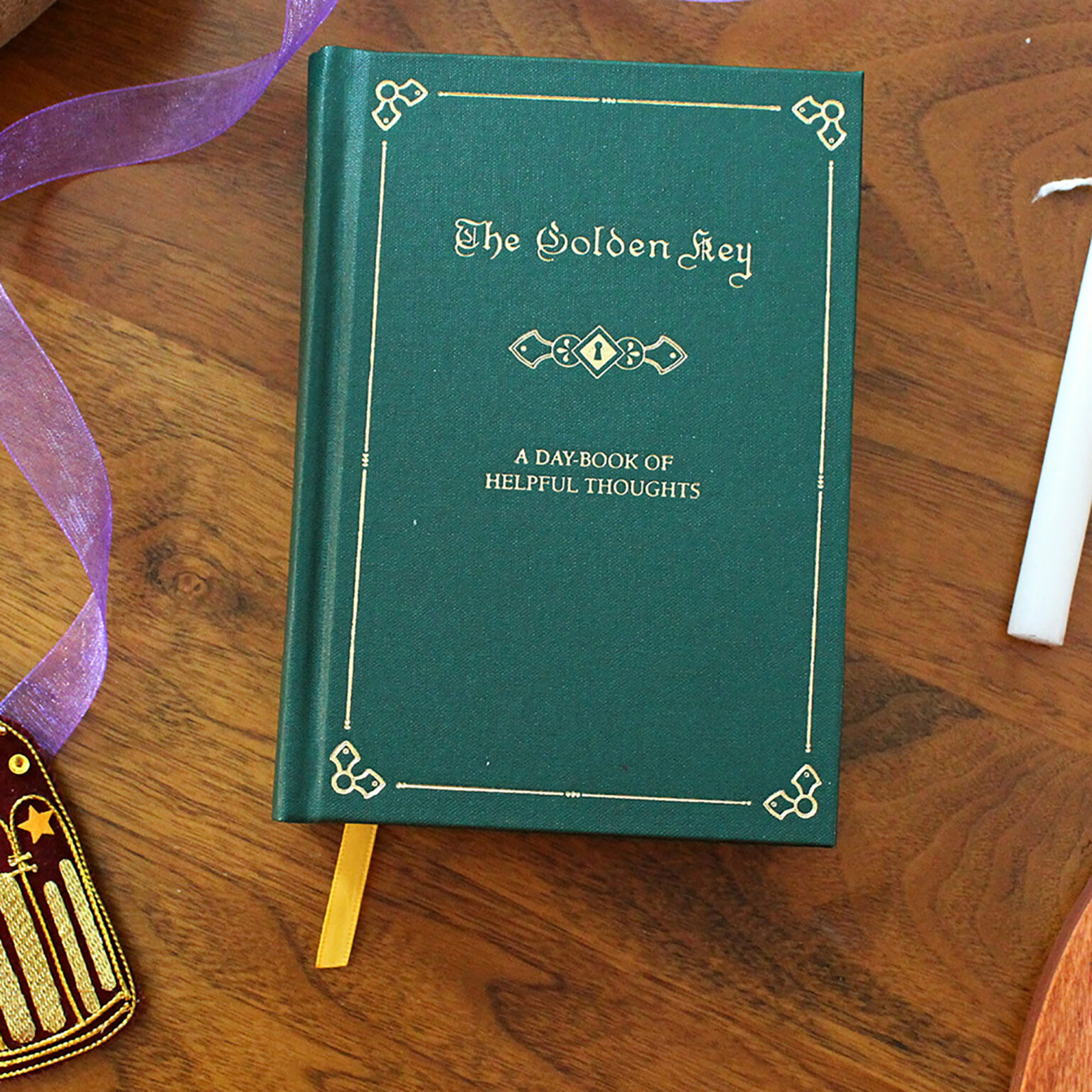 Green hardcover book titled 'The Golden Key' with gold decorative border, placed on a wooden table with purple ribbon nearby and a yellow bookmark showing.