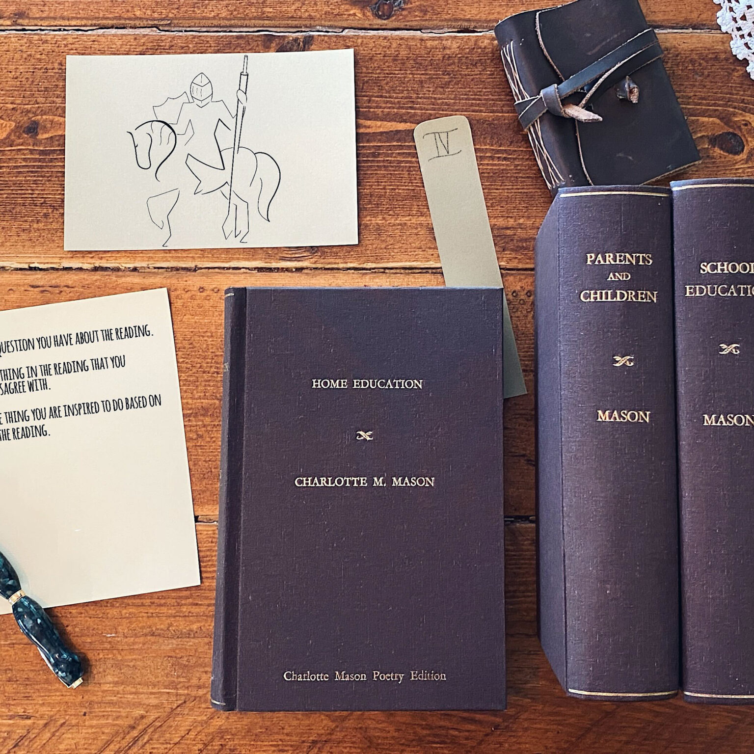 Dark blue volumes titled 'Charlotte Mason Poetry Edition' on a wooden table, with a small sketch card of a knight on a horse nearby.