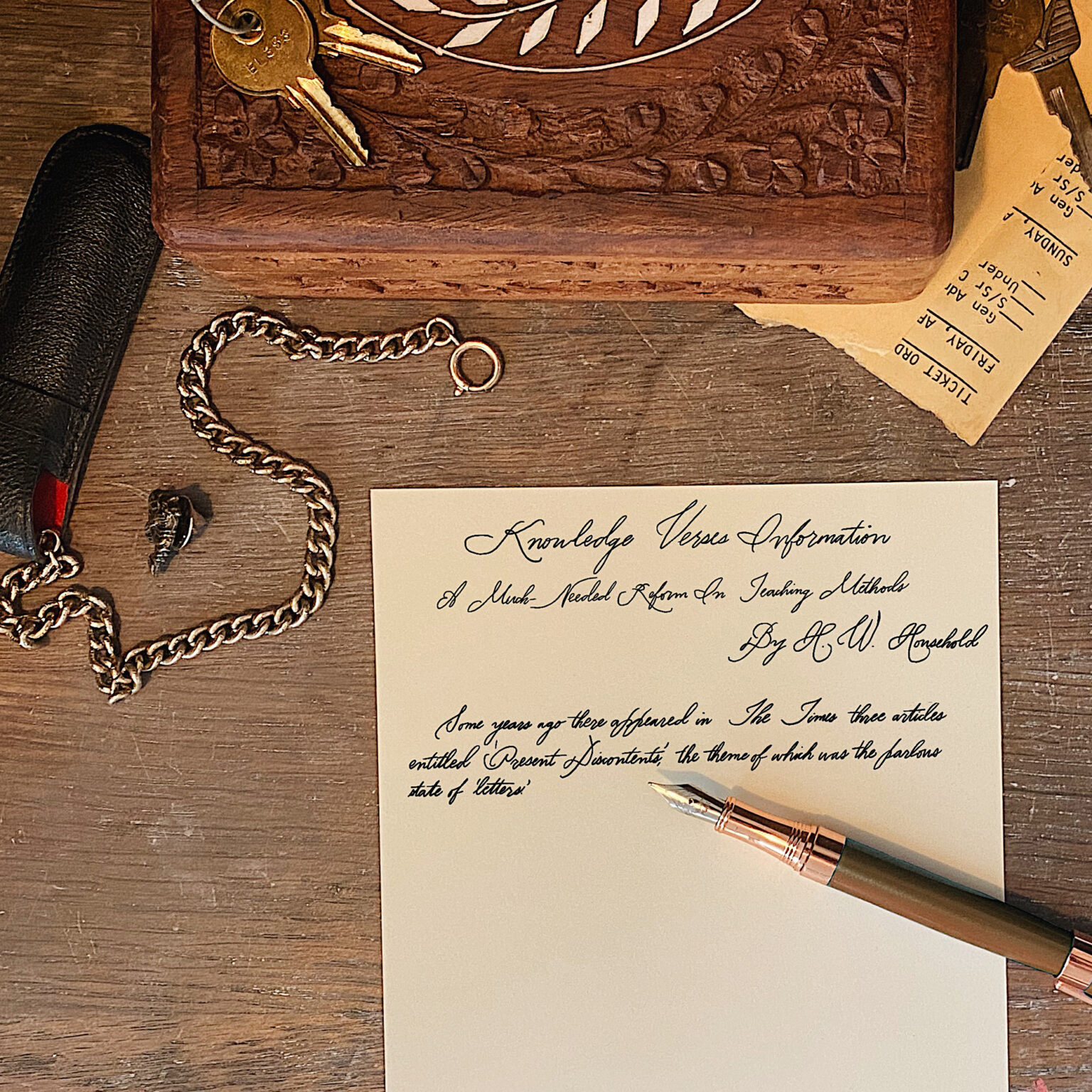 Ornate carved wooden box with keys on a rustic desk, alongside a metal chain and handwritten manuscript with a fountain pen nearby.