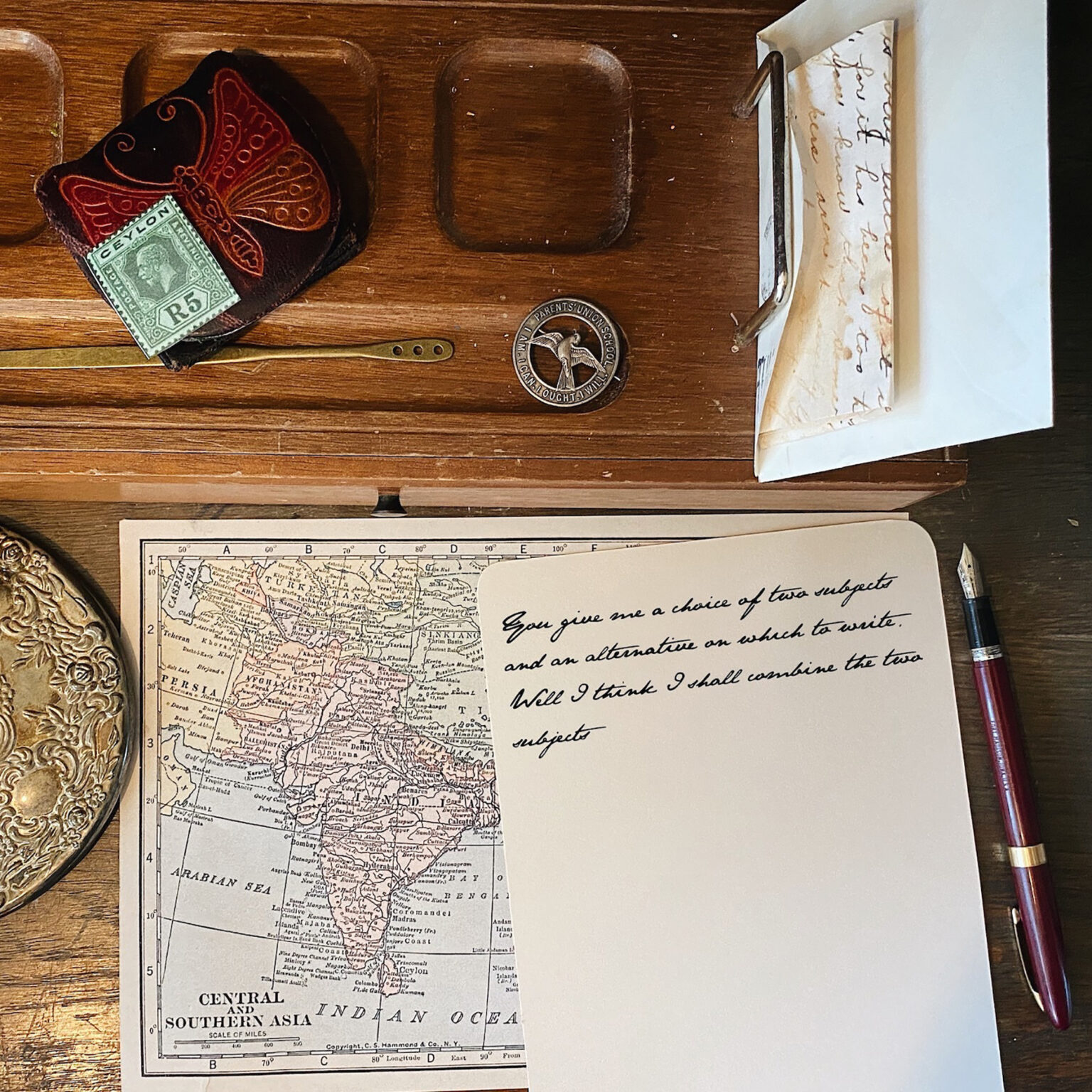 Vintage desk scene with a map of Central and Southern Asia, a green Ceylon stamp, and a leather item featuring a red butterfly design.
