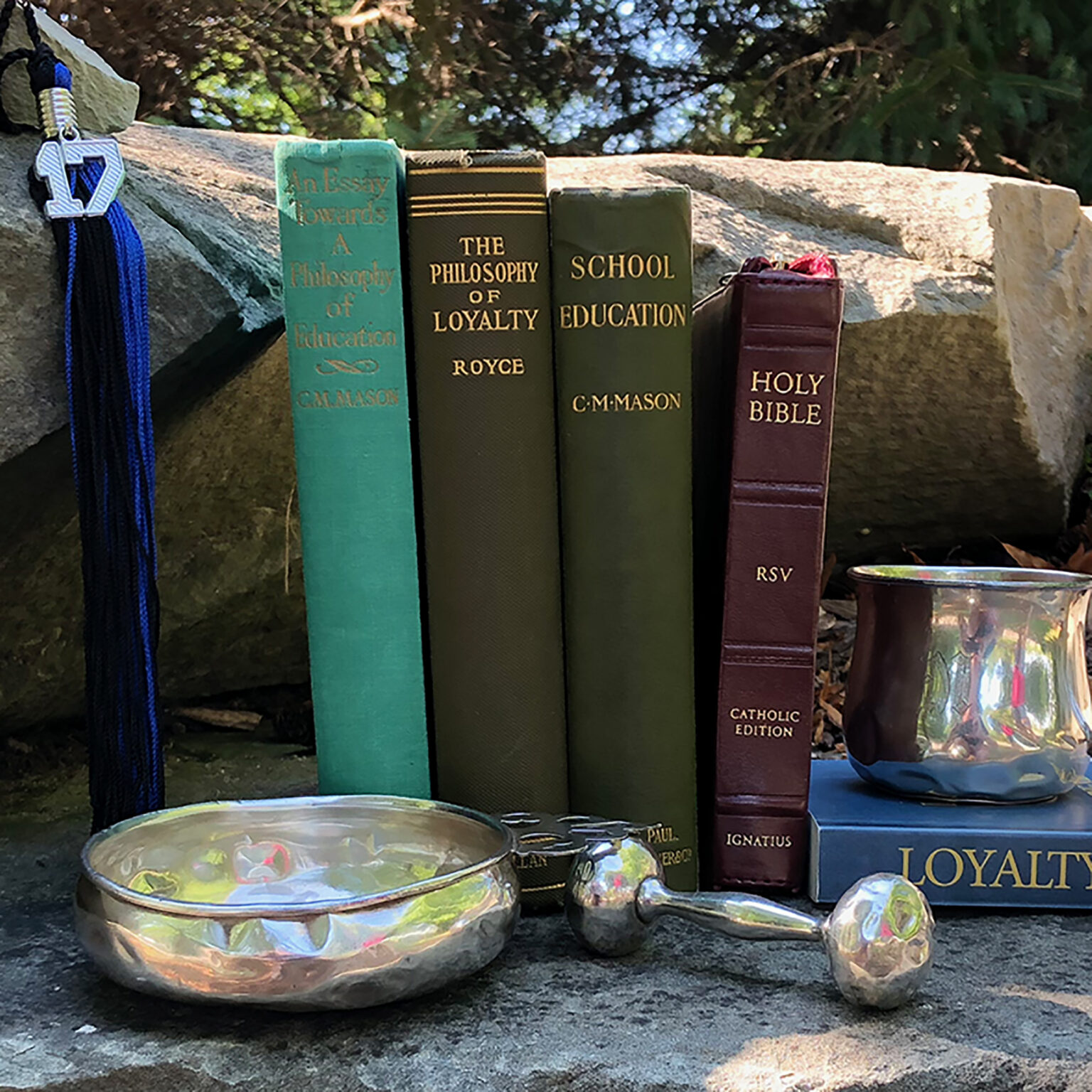 Row of academic books on a stone ledge with a blue graduation tassel and a decorative glass bowl nearby.