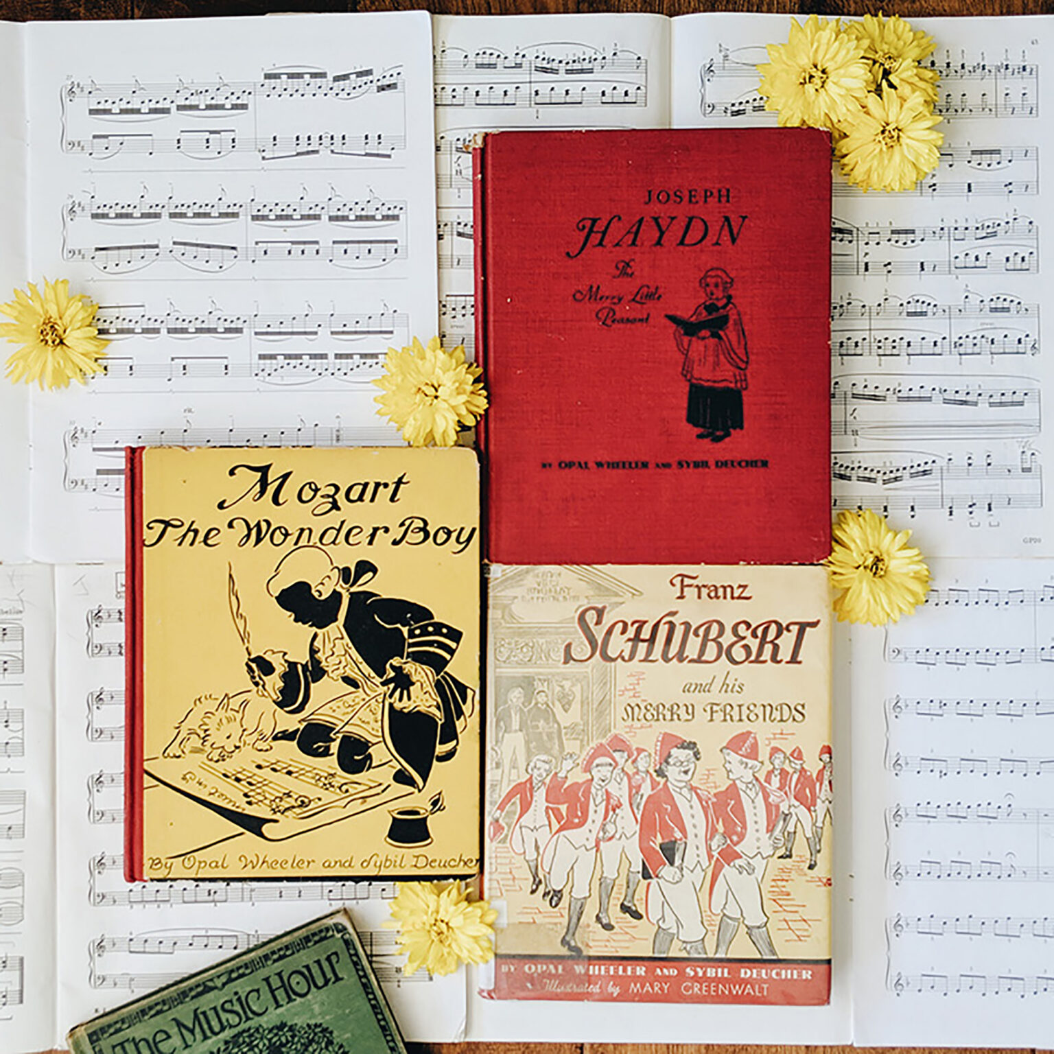 Open sheet music pages topped with vintage red Haydn book and bright yellow flowers in a still-life arrangement.