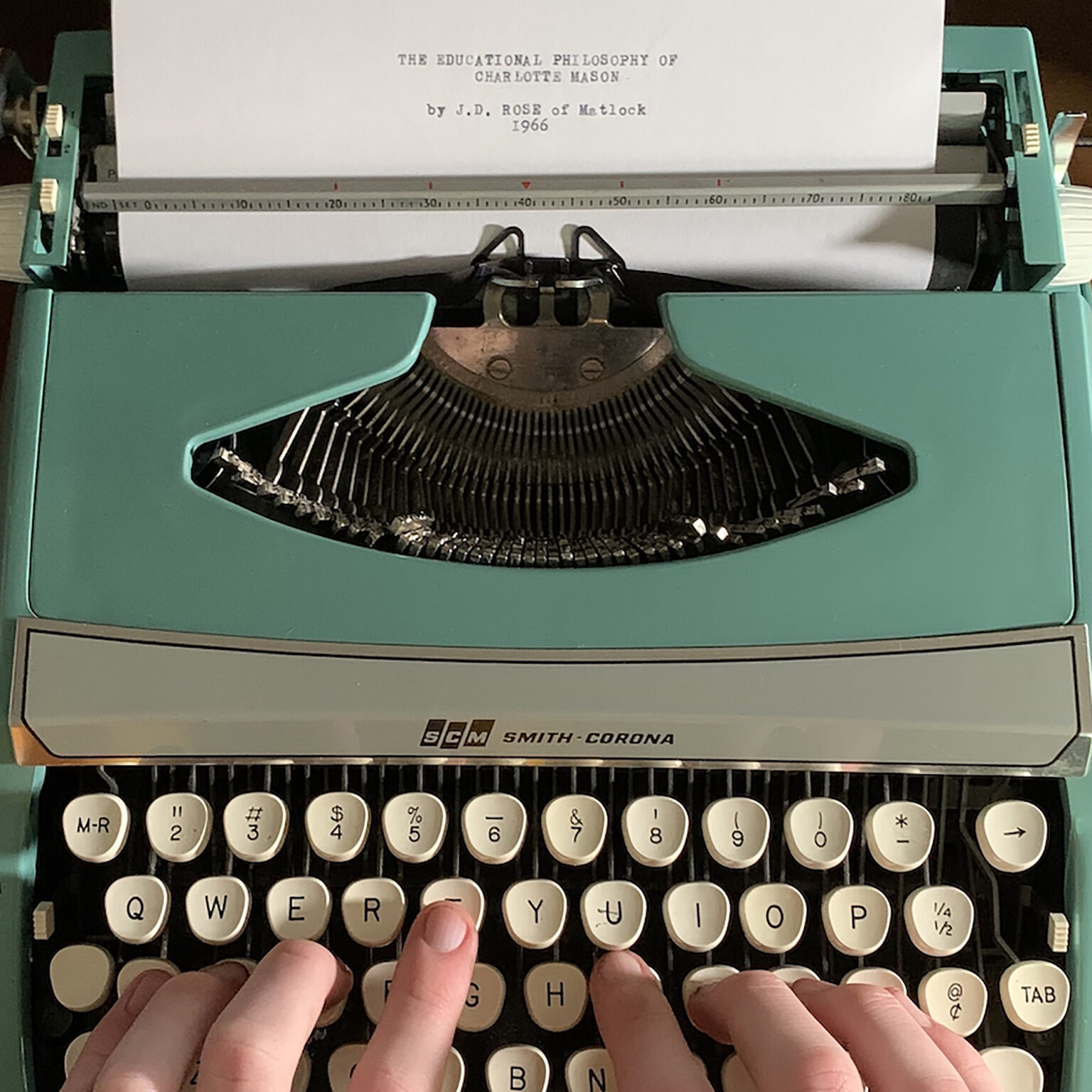Green vintage Smith-Corona typewriter in use, hands typing on round white keys with a sheet of paper above.