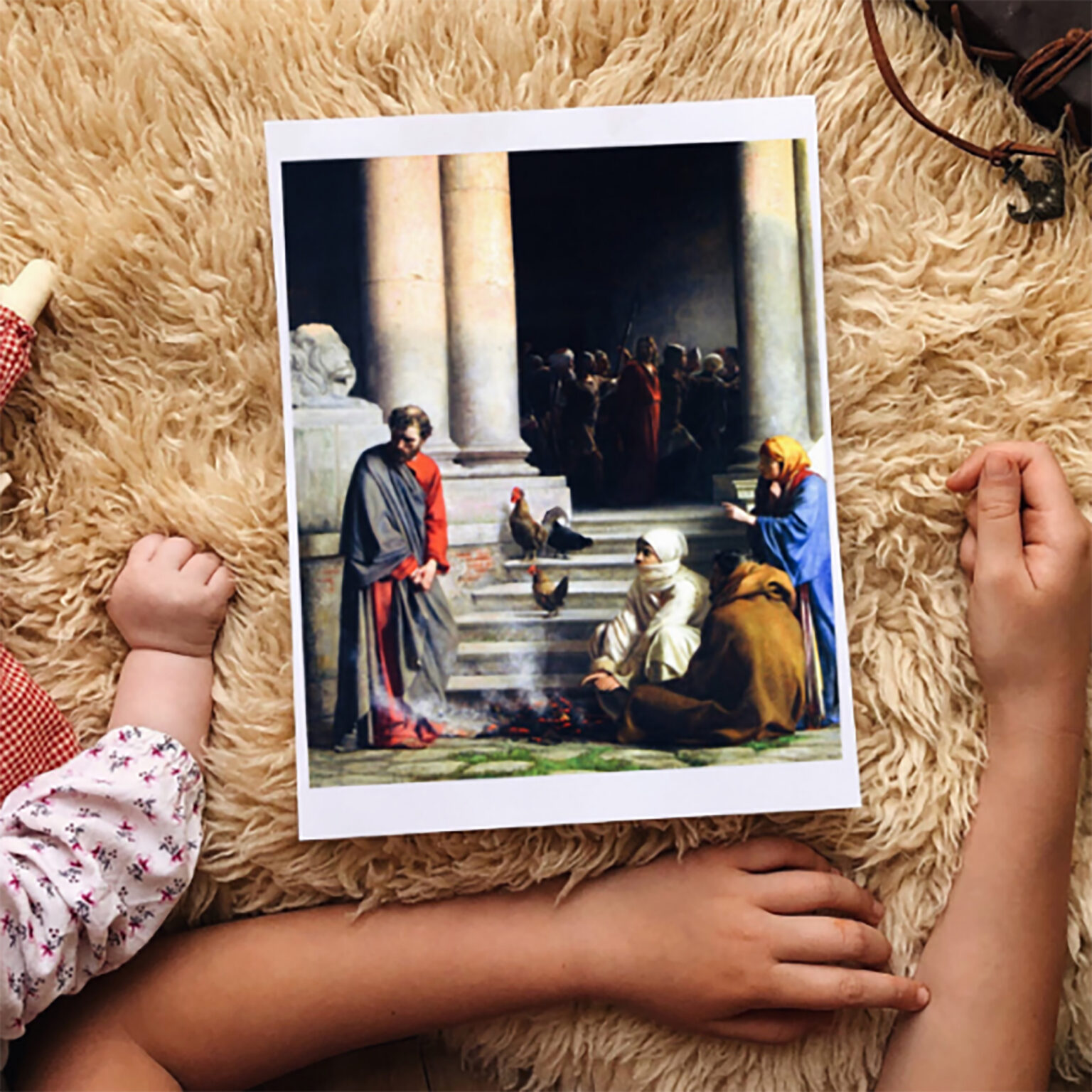 Postcard of The Last Supper resting on a fluffy beige rug, held by a child’s arms.