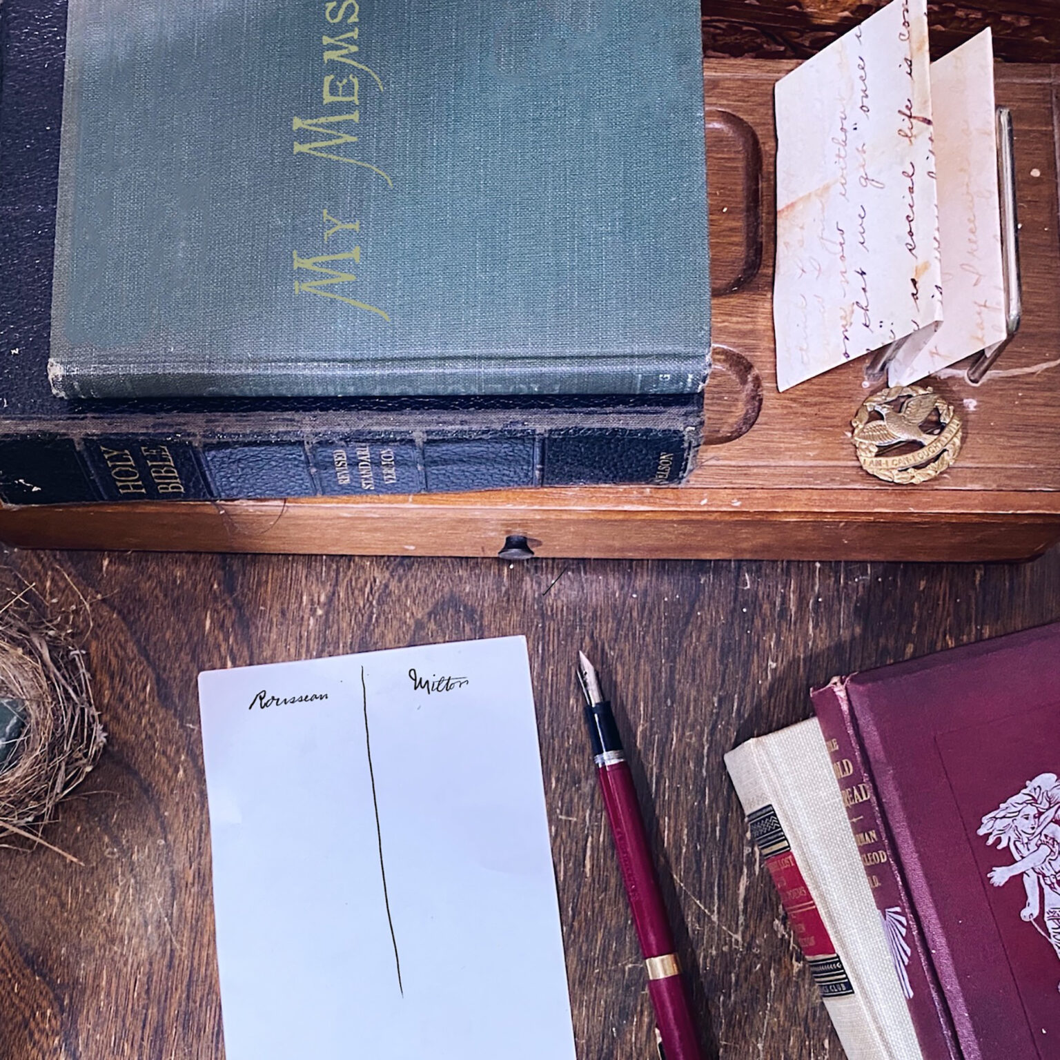 Antique books on a wooden desk with handwritten letters on loose sheets and a red pen nearby.