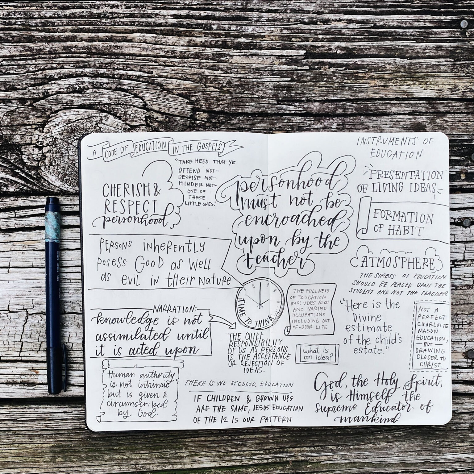 Open notebook with handwritten, artistic lettering on a weathered wooden table, a marker at the left edge nearby.