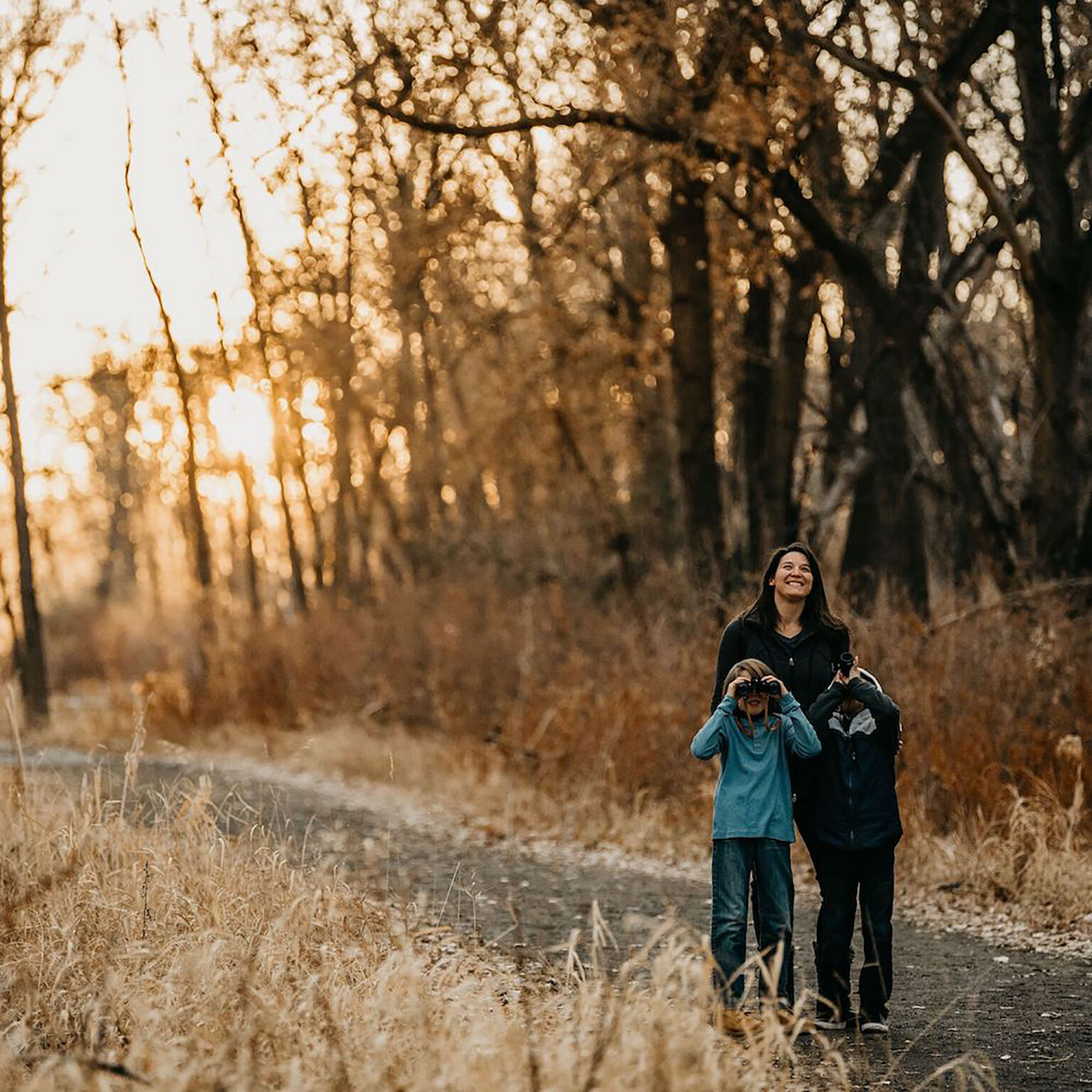People stand in a sunlit, grassy field, smiling while a child in front holds a camera.
