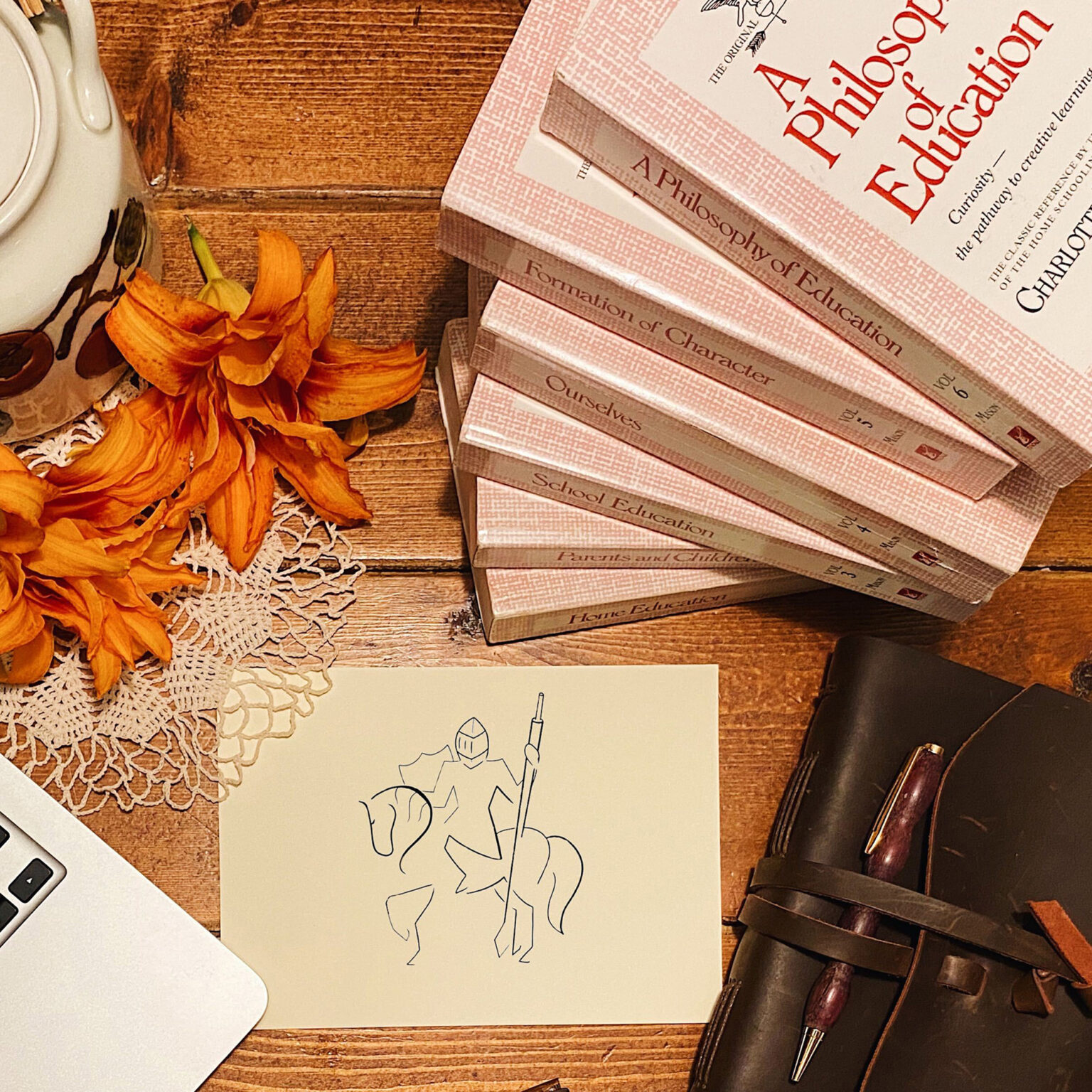 Stack of pink Philosophy of Education books beside orange autumn flowers on a wooden desk