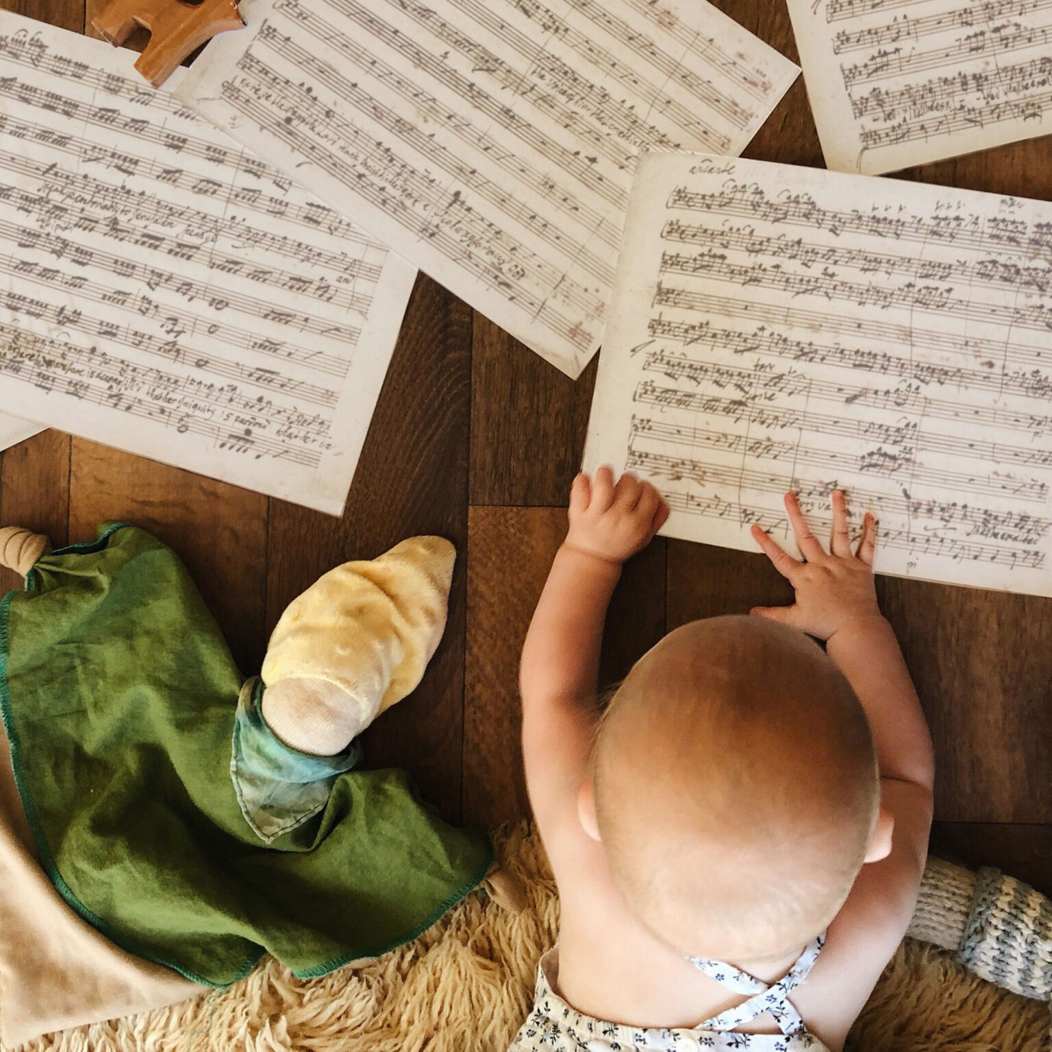 Overhead view of children sitting on a wooden floor with scattered handwritten music sheets around them.