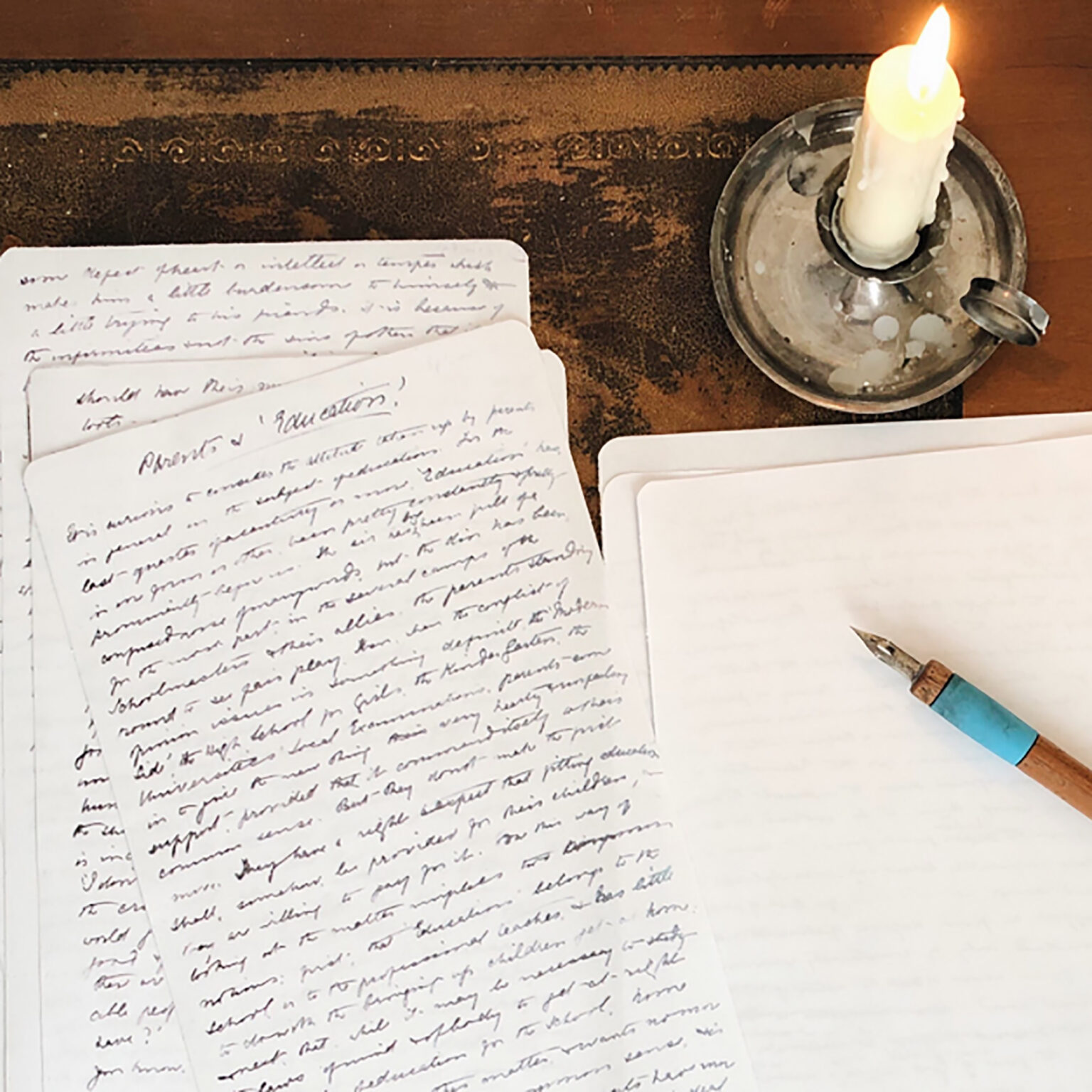 Handwritten notebook pages with cursive notes on a dark wooden desk, a lit candle in a metal holder nearby, and a fountain pen resting on the edge of the page.