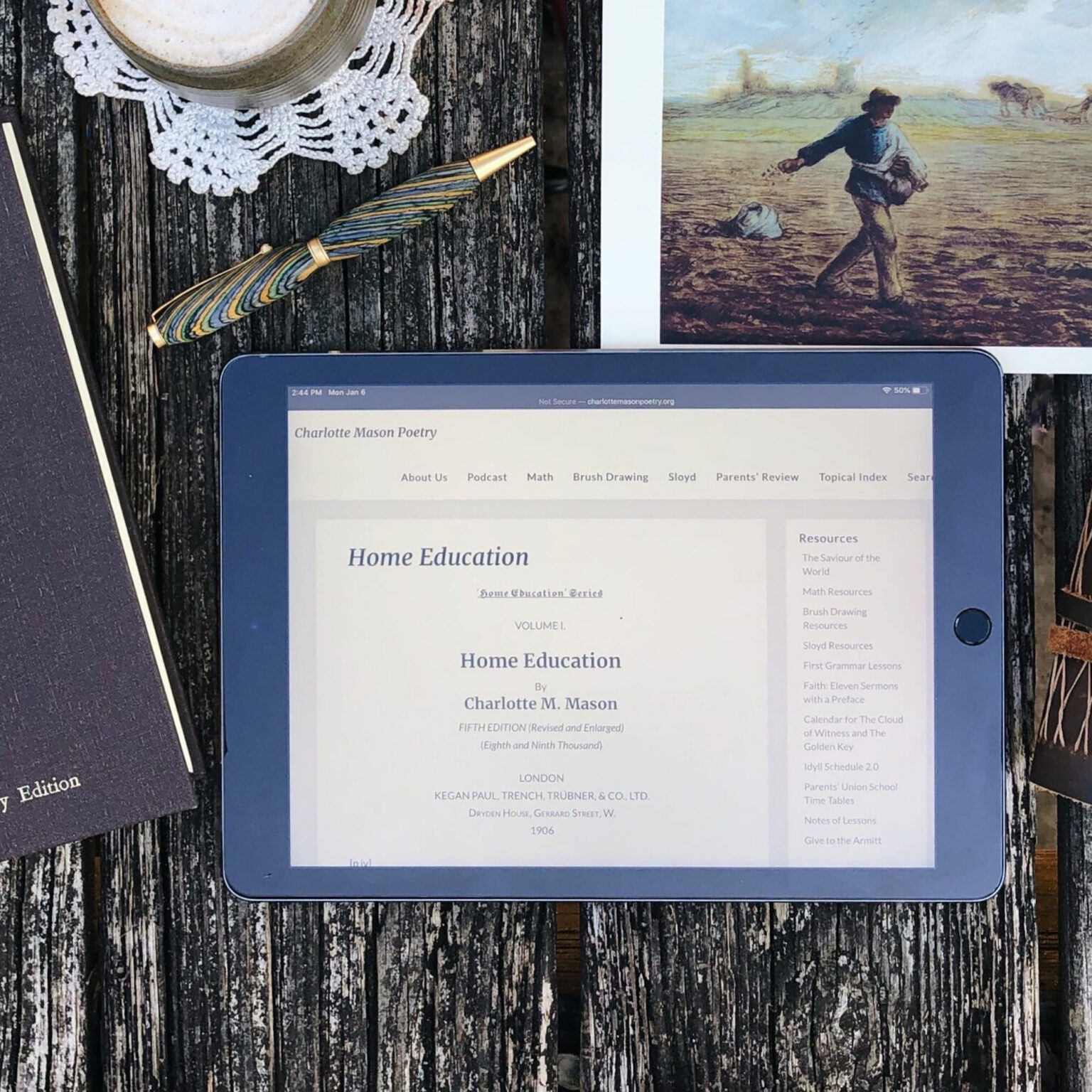 Tablet showing the Charlotte Mason Poetry website on a wooden table, with a striped fountain pen and a lace doily nearby.