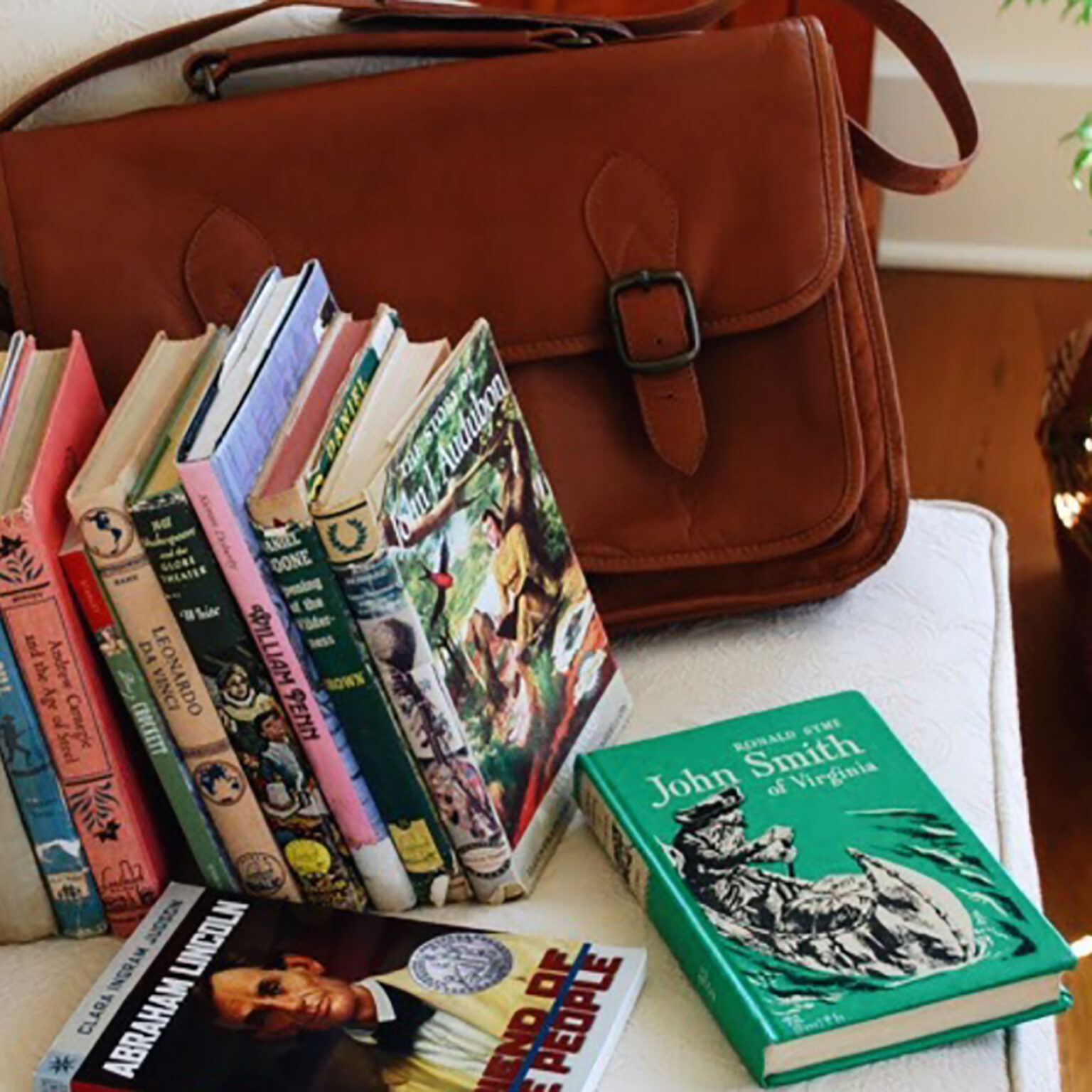 Brown leather satchel resting on a shelf with colorful children's books lined upright beside it.