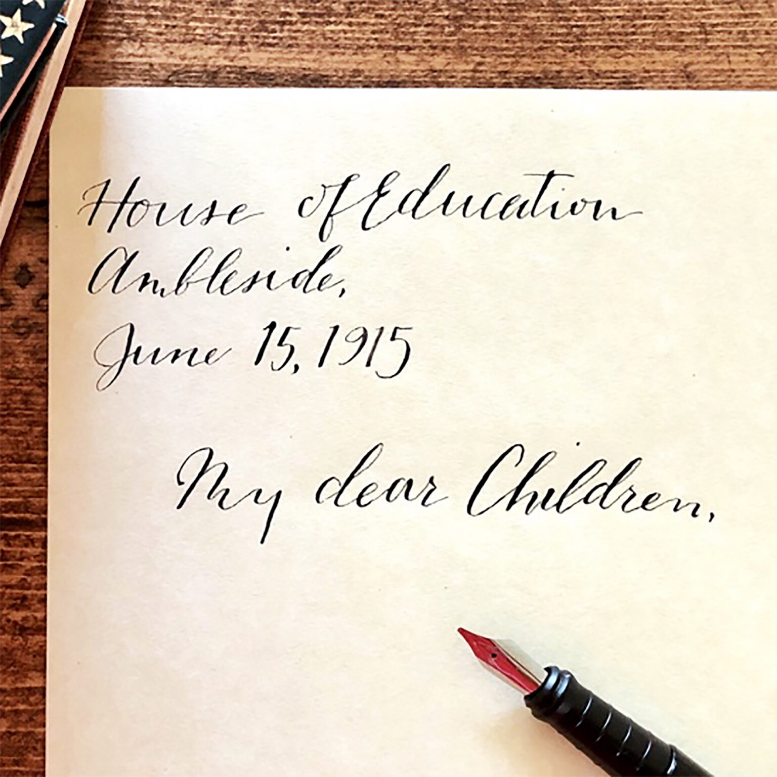 Close-up of a paper with elegant cursive handwriting reading 'House of Education Outside,' and a red-and-black fountain pen in the corner.