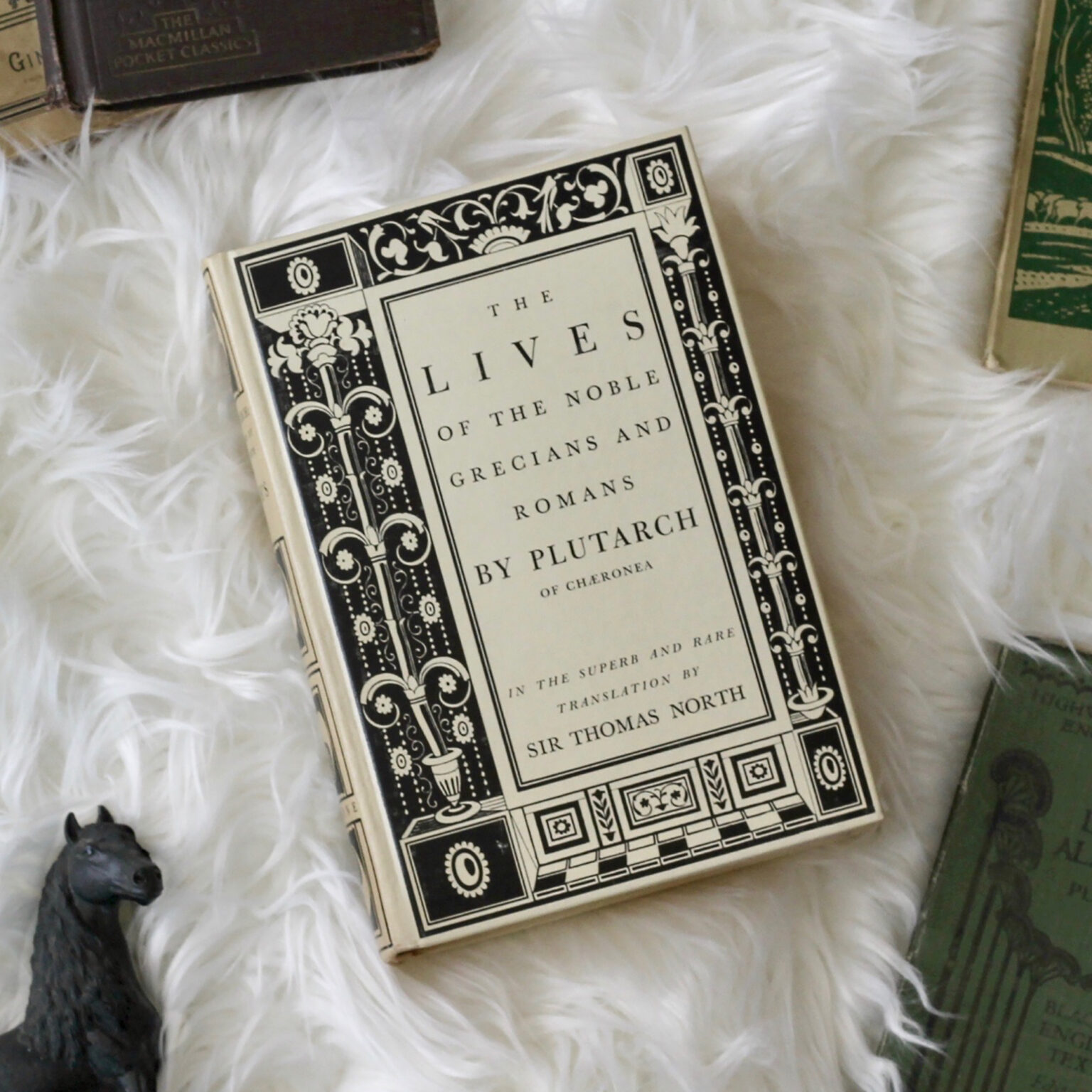 Hardcover ornate edition of The Lives of the Noble Greeks and Romans by Plutarch on a white fluffy surface.