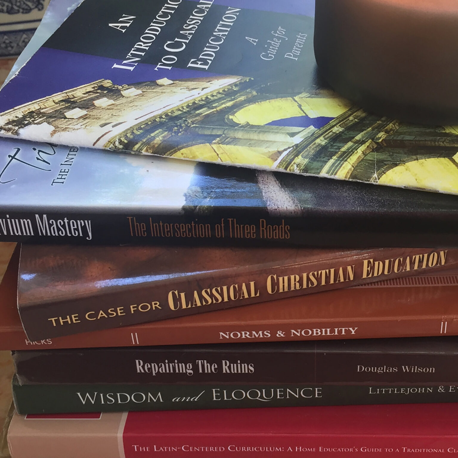 Stacked textbooks about classical Christian education, with visible titles like The Case for Classical Christian Education and Wisdom and Eloquence along with other related volumes.