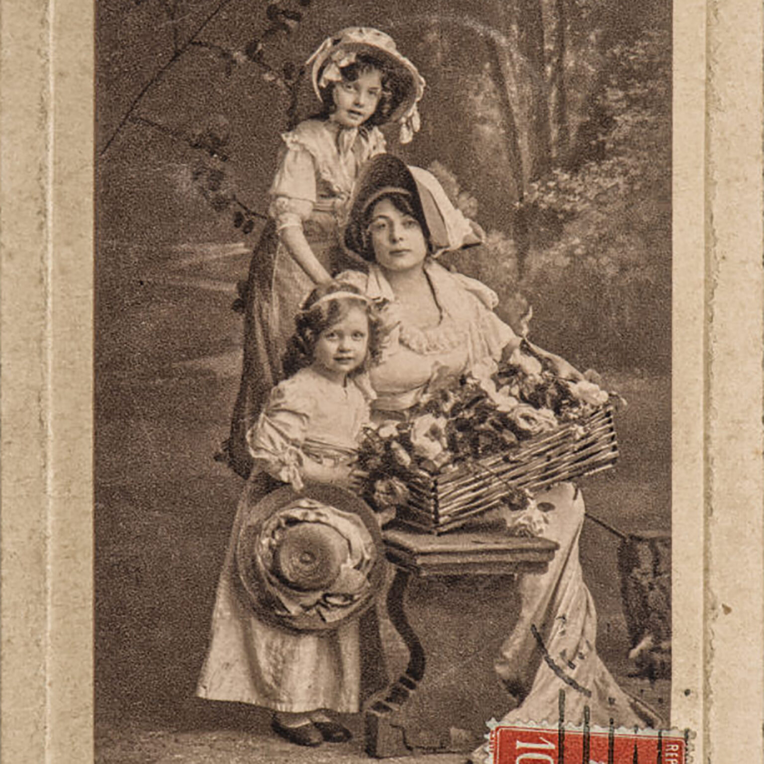 Vintage sepia photo of a woman seated with a large bouquet, a child on her lap, and another child standing behind them in period clothing.
