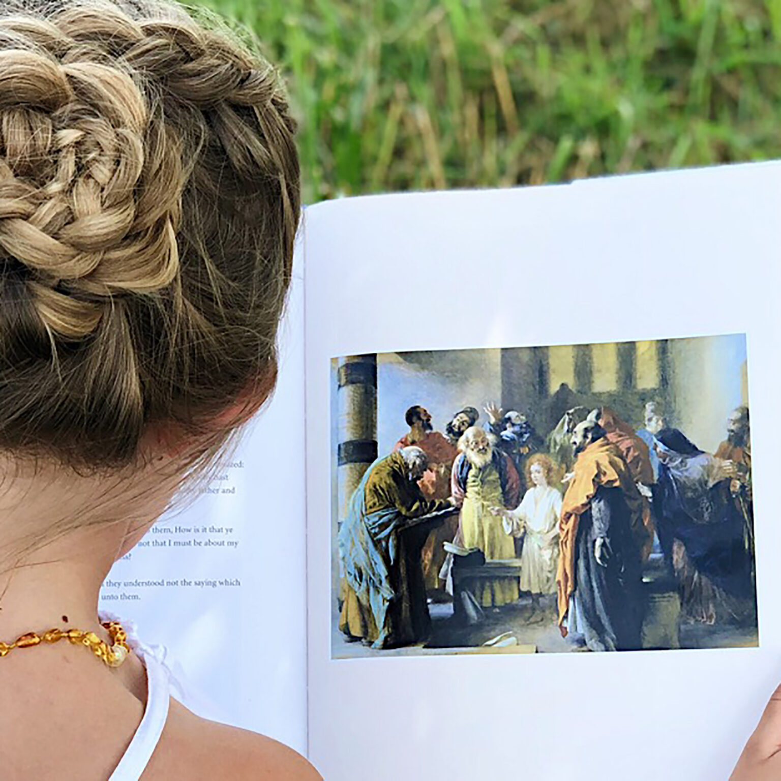 Close-up of a person with braided blonde hair reading an open magazine outdoors.
