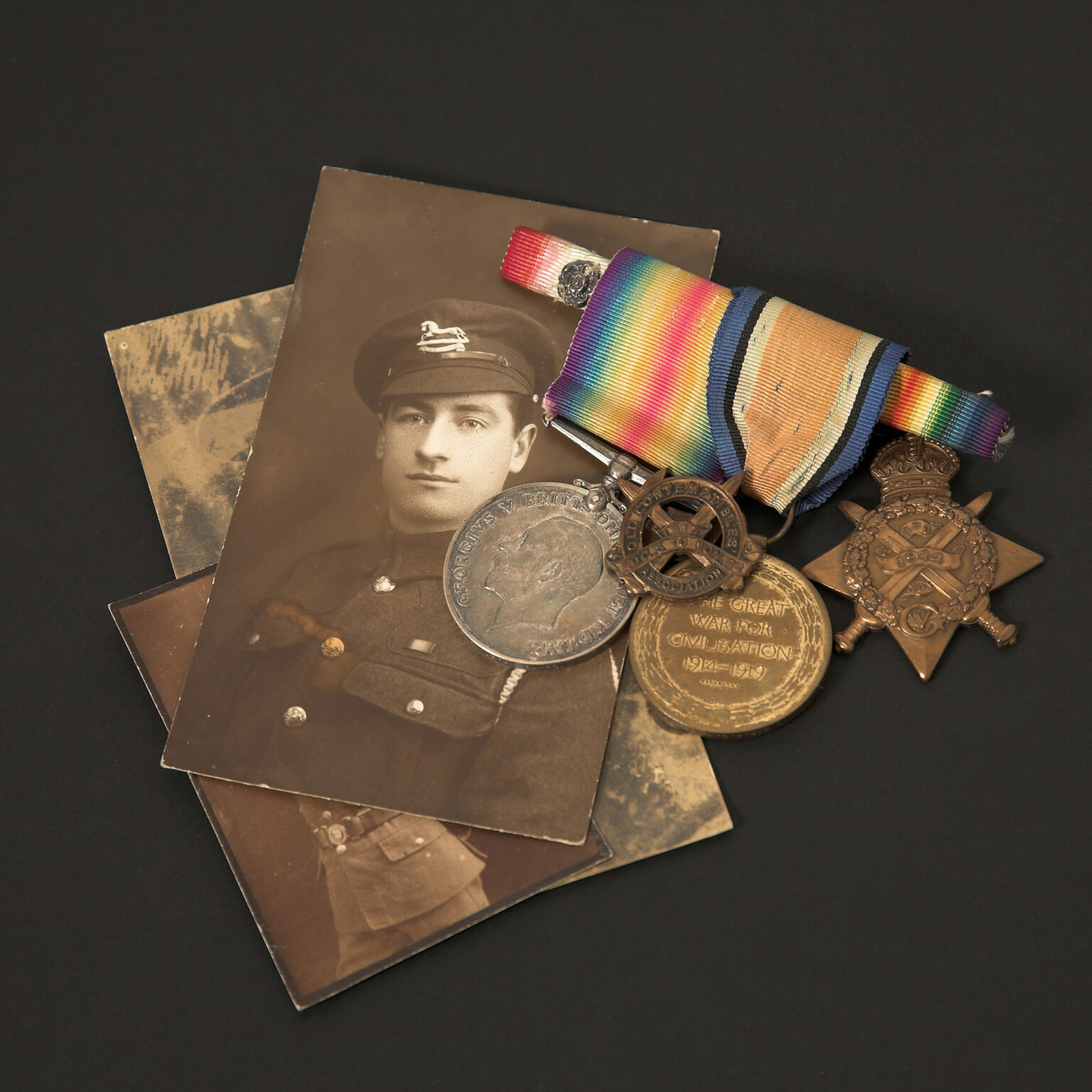 Old sepia-toned photos partially covered by a rainbow ribbon and several bronze medals on a dark background.