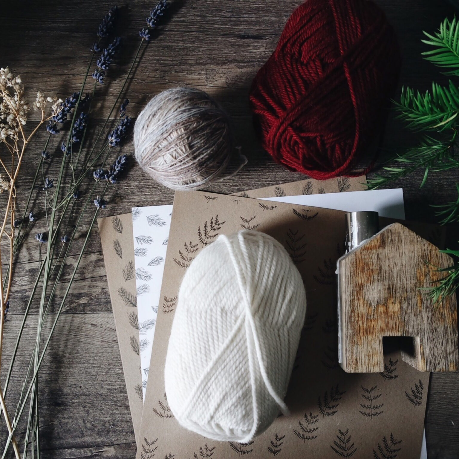 Flat lay of craft supplies on a wooden table: lavender stems, pale twine, red yarn, white yarn, and stamped kraft cards.