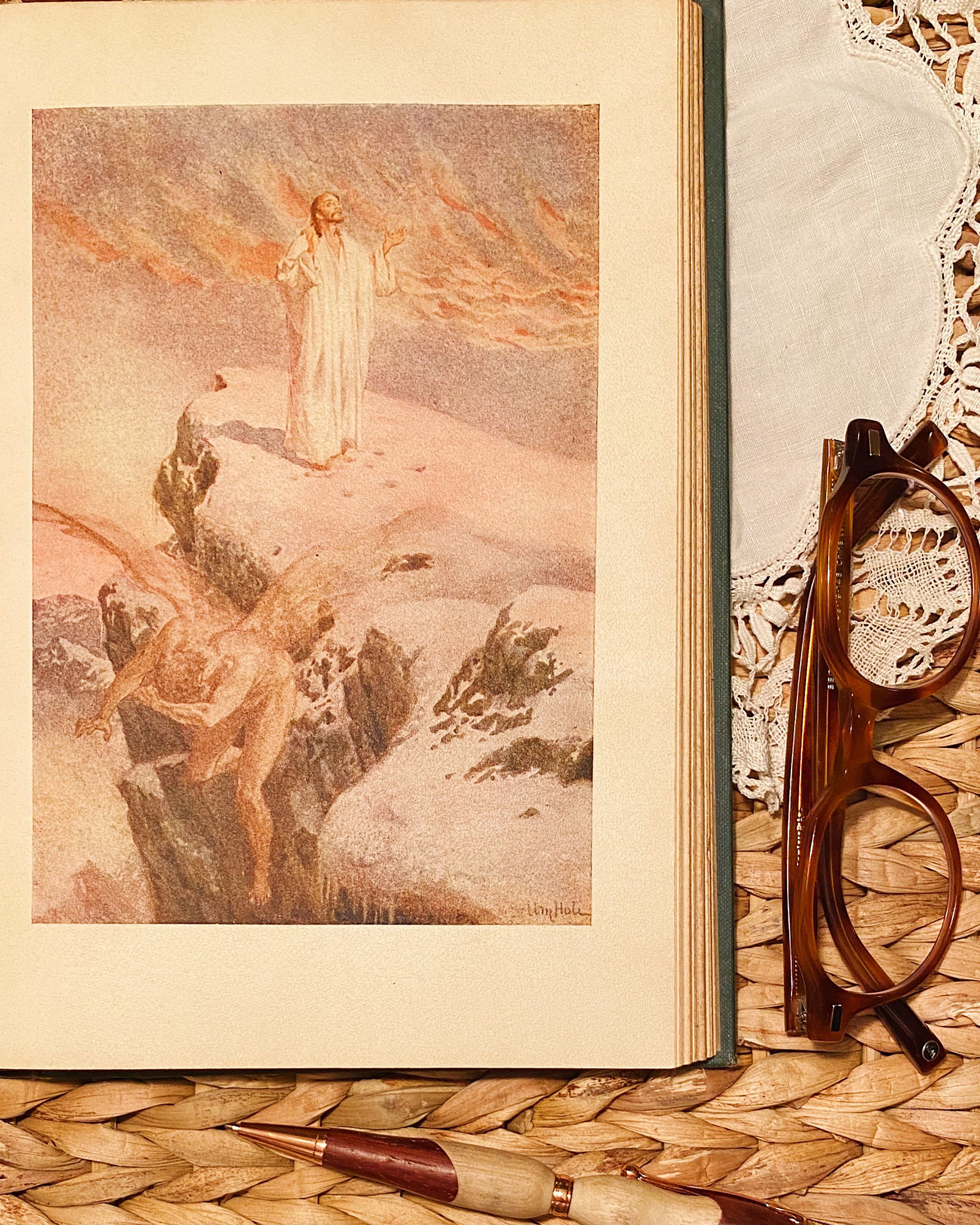 Open book displaying a pastel illustration of a bearded man in white robes standing on a rocky cliff, with glasses to the right.