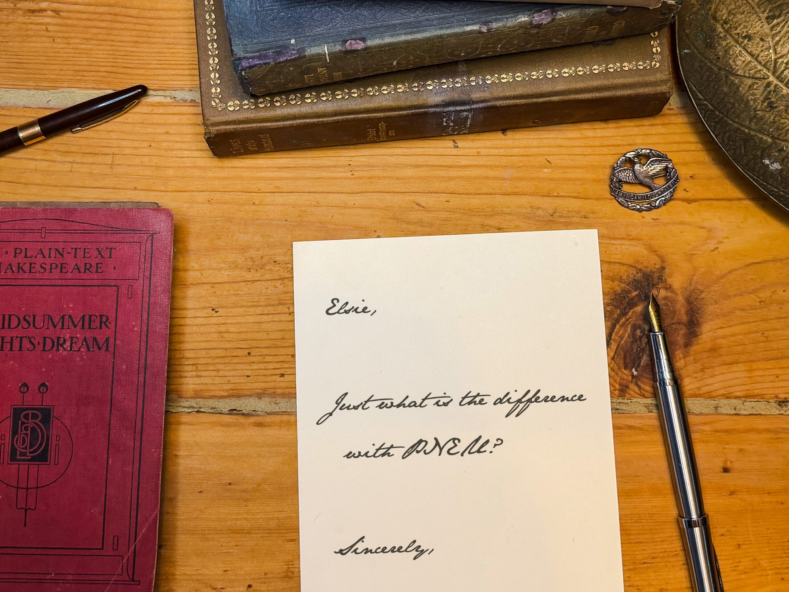 Vintage desk scene with old books, a fountain pen, and a handwritten note reading 'Elsie,' on a wooden surface.
